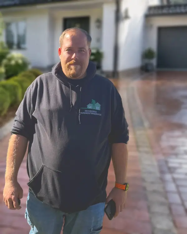 Pascal Rechburg, Inhaber von Rechburgs Hausmeisterservice, im Firmen-Hoodie; der Hintergrund mit Wohnhaus und Einfahrt ist KI-generiert