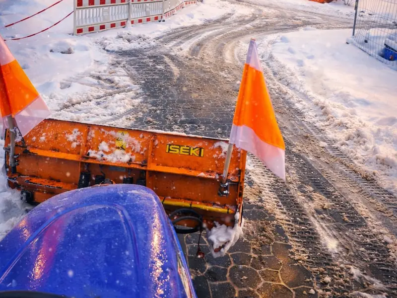 Räumschild mit Warnfahnen auf frisch geräumter Pflasterzufahrt im Schnee